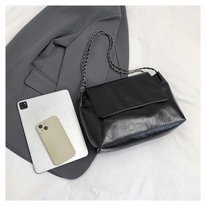 Sac bandoulière en cuir froissé noir avec chaîne posé à côté d'une tablette et d'un mobile