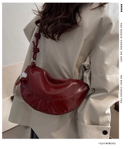 Détail du sac croissant rouge foncé avec bandoulière nouée et charm porté par mannequin