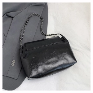 Détail de la texture cuir verni noir et de la bandoulière chaîne argentée du sac chic