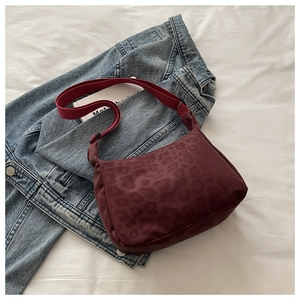 Detail of burgundy leopard print crossbody bag with adjustable strap on denim background