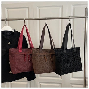 Three leopard print tote bags in burgundy, brown and black hanging on a metal rack