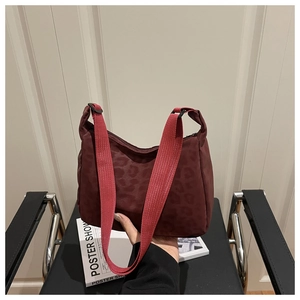 Detail of burgundy leopard print tote bag with wide red fabric strap held by hand