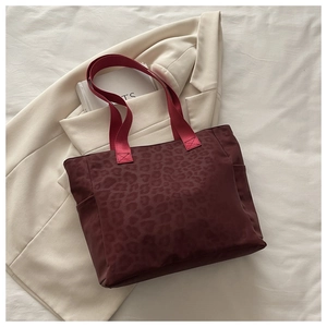 Détail du sac cabas léopard avec anses rouges sur fond de tissu blanc texturé