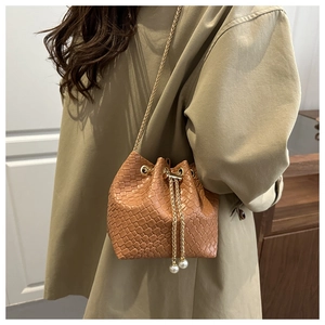Detail of brown woven bucket bag featuring gold chain strap and pearl drawstring tassels