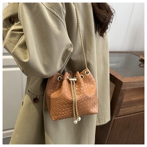 Detail of caramel brown woven leather bucket bag with gold chain and pearl drawstrings