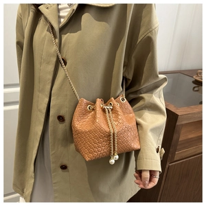 Detail of brown woven bucket bag with gold chain strap and pearl accents on drawstring