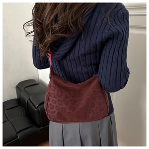 Deep red crescent shoulder bag with leopard pattern texture on blue sweater