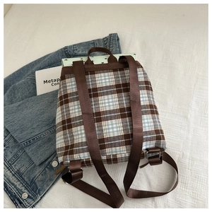 Detail of classic plaid backpack with brown fabric straps on a textured white surface