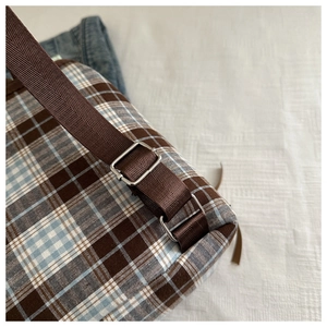 Detail of mint green plaid backpack showing nylon straps and adjustable silver buckles