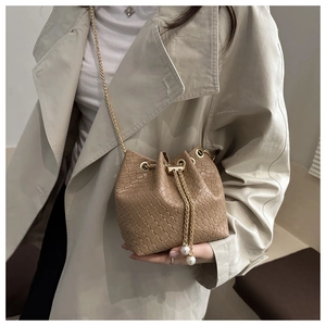 Detail of khaki bucket bag with gold chain and pearl pendants on beige coat