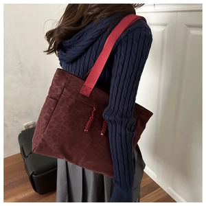 Détail du sac cabas bordeaux à motif léopard avec bandoulière rouge et pompon décoratif