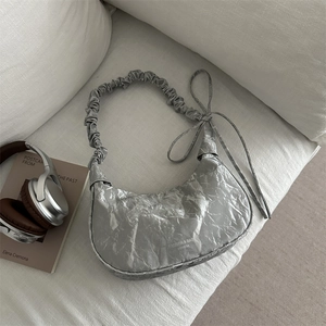 Silver metallic crescent underarm bag with pleated strap and bow on white cloth