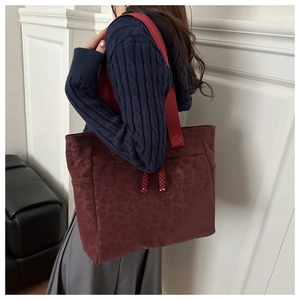 Detail of burgundy leopard embossed tote bag with wide strap and woven tassels
