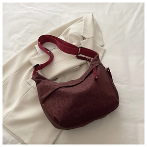Détail d'un sac bandoulière léopard bordeaux posé sur une veste élégante