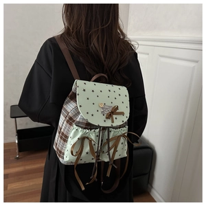 Detail of mint green bow backpack with check pattern and black star accents on a model