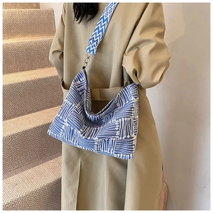 Detail of blue and white geometric knit bag with wide wavy shoulder strap and metal buckle