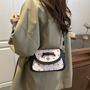 Sac bandoulière rose avec nœuds noirs et pendentif cœur porté à l'épaule par le modèle