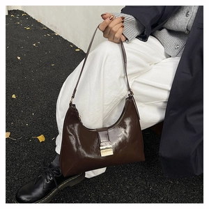 Outdoor shot of a glossy dark brown underarm bag with gold buckle and leather strap