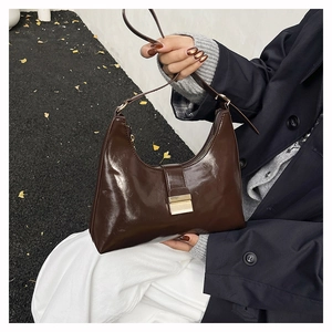 Detail of dark brown glossy leather hobo bag with gold metal clasp and crescent shape