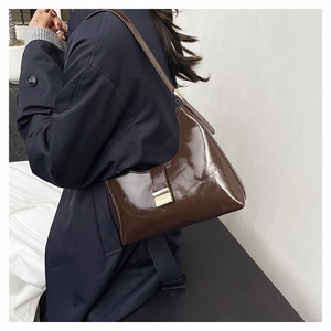 Detail of a brown polished leather shoulder bag featuring a gold square buckle and strap
