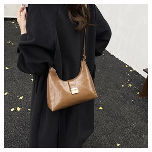 Close-up of caramel brown crescent shoulder bag with golden metallic buckle in autumn setting
