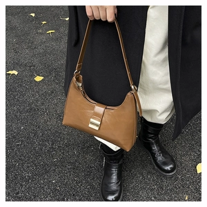 Outdoor close-up of a caramel leather dumpling bag with a golden metallic buckle