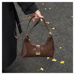 Detail of dark brown polished leather croissant bag with gold buckle on autumn leaves