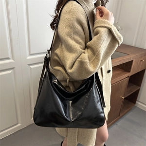 Borsa sottospalla nera lucida con tracolla regolabile indossata da una modella in stile minimal