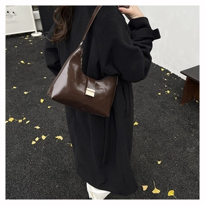 Detail of dark brown patent leather hobo bag with gold buckle on black coat