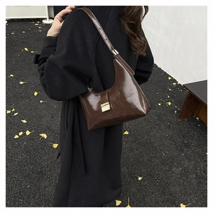 Detail of dark brown glossy shoulder bag with a gold buckle worn with a black wool coat