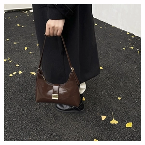 Detail of dark brown glossy hobo bag with gold buckle shown in a lifestyle autumn setting
