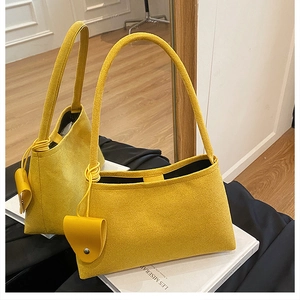 Détail du sac à bandoulière en daim jaune avec breloque cœur posé sur un livre