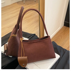 Gros plan d'un sac à main rétro en daim marron foncé avec pendentif sur un livre