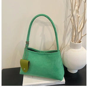 Detail view of a bright green felt shoulder bag with a heart charm on a book