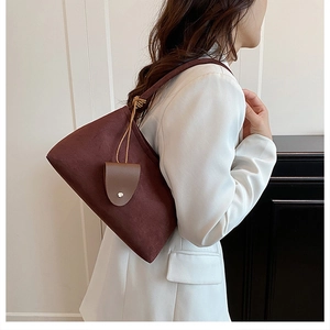 Detail of burgundy suede shoulder bag with brown leather strap and decorative pendant