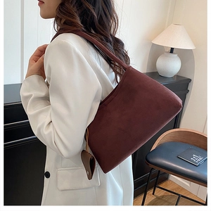 Détail d'un sac bandoulière en daim bordeaux avec breloque cœur porté sur un blazer blanc