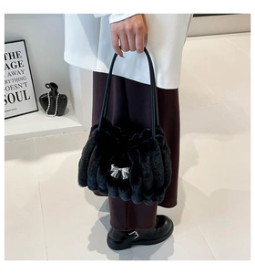 Détail du sac à main en peluche noire avec nœud argenté sur texture fausse fourrure