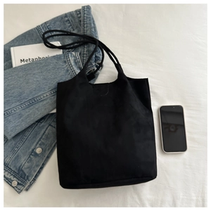 Minimalist black tote bag detail with smooth flap design on a white textured background