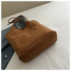 Flat lay of a brown suede bucket tote bag next to a denim jacket on white fabric