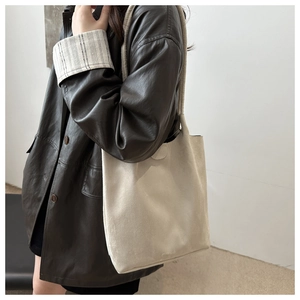 Side view of a large cream suede tote bag worn by a model in a dark brown leather coat