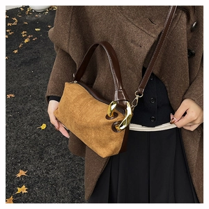 Detail of a brown suede cylinder bag with gold chain strap on a wool coat outfit