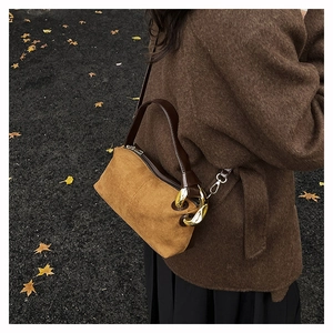 Detail of ginger suede handbag with leather straps and gold chain on autumn ground