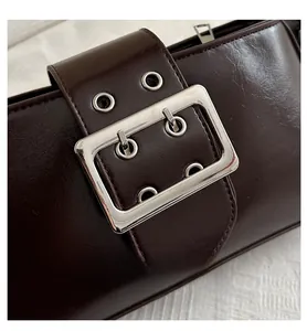 Gros plan sur un sac en cuir marron foncé brillant avec boucle argentée et œillets
