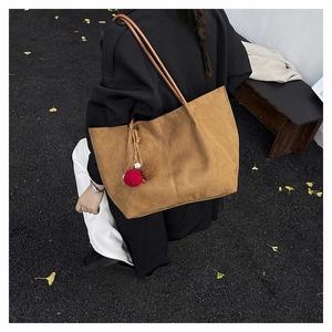 Brown frosted tote bag with pompom charm shown on a street with autumn ginkgo leaves