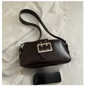 Sac sous le bras en cuir marron foncé avec grande boucle argentée à côté d'un smartphone