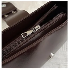 Détail du sac en cuir marron foncé montrant les zips argentés et les compartiments doubles