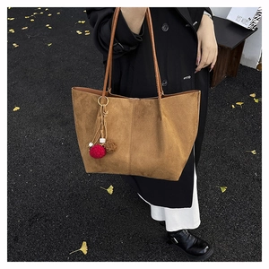 Close-up of brown suede tote bag with pompom charm on a scenic autumn street