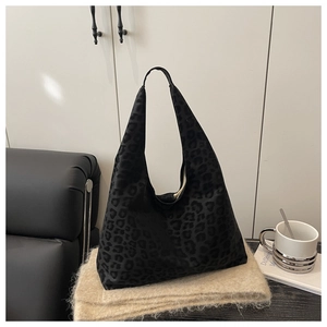 Close-up of black leopard print hobo tote bag on beige textured blanket background