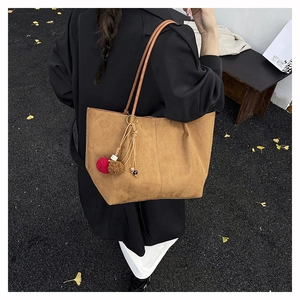 Close-up of brown suede tote bag featuring plush pompom charms and minimalist design