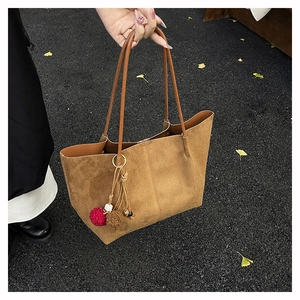 Detail of a brown suede tote bag with plush charm on a seasonal autumn street